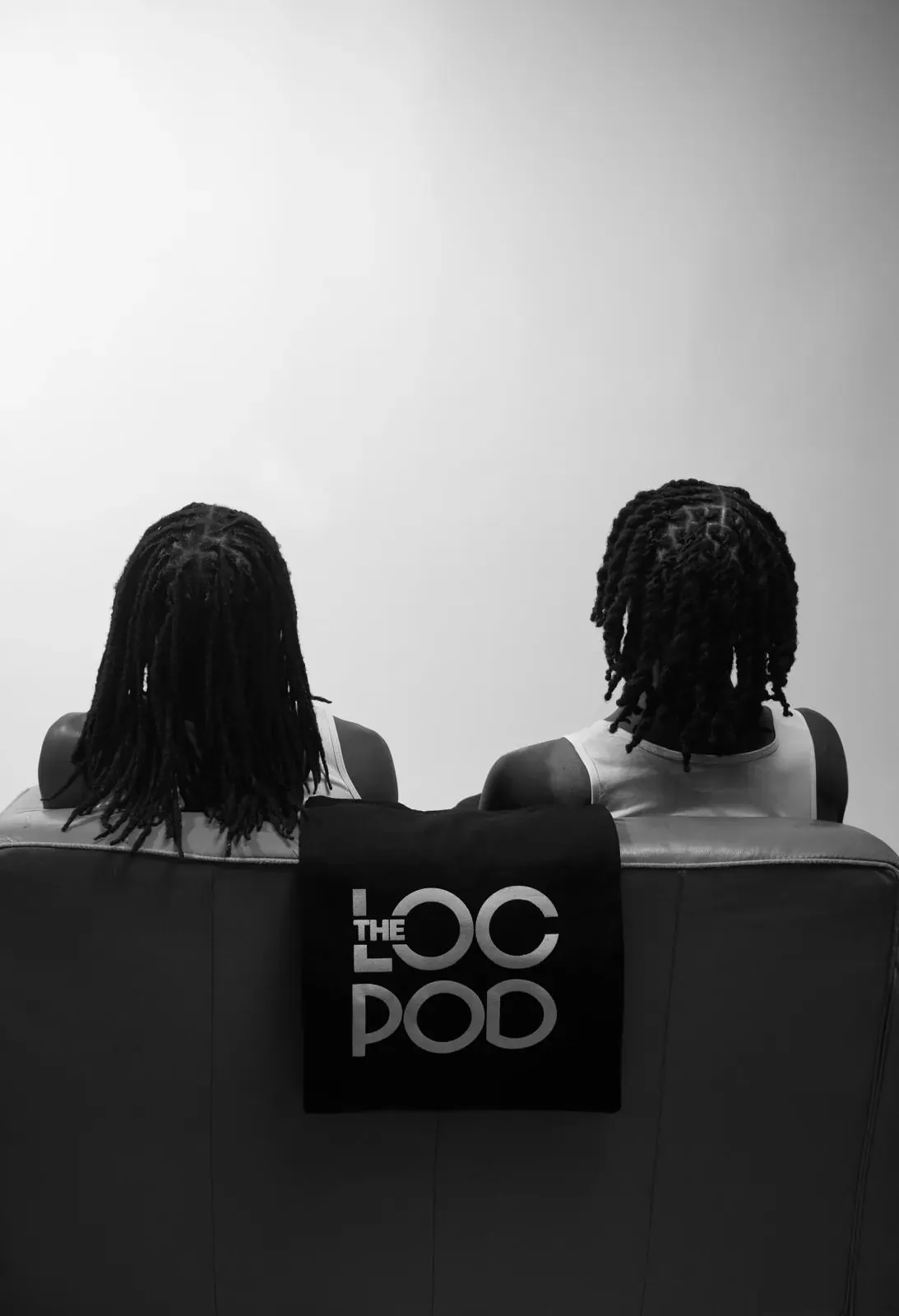 Two people with locs seen from behind on a leather sofa, a LocPod tote draped between them